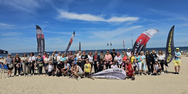 Uczestnicy imprezy Plażowy Nordic Walking w Świnoujściu maszerują z kijami po plaży nad Bałtykiem, na czele z Prezydent Joanną Agatowską.