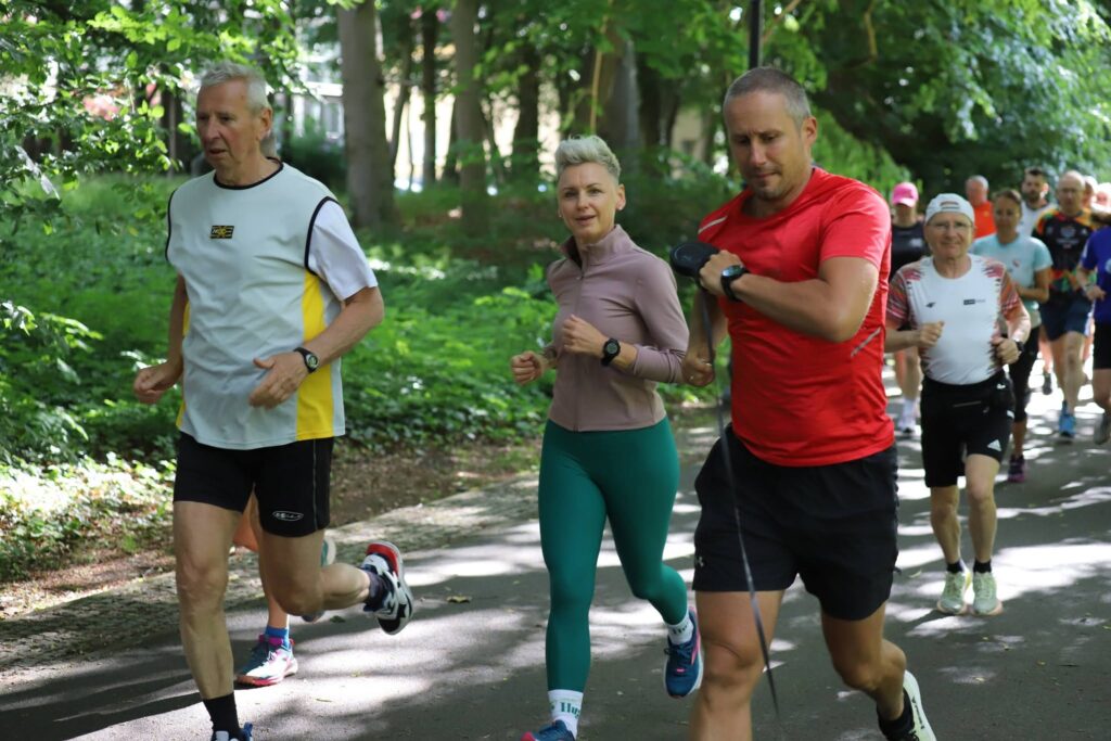 Uczestnicy 452. parkrun Świnoujście biegnący w słoneczny poranek w Parku Zdrojowym.