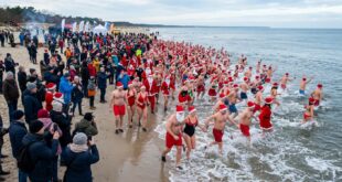 Morsujący Mikołajowie w czerwonych czapkach wchodzący do zimnego Bałtyku na plaży w Świnoujściu