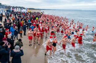 Morsujący Mikołajowie w czerwonych czapkach wchodzący do zimnego Bałtyku na plaży w Świnoujściu