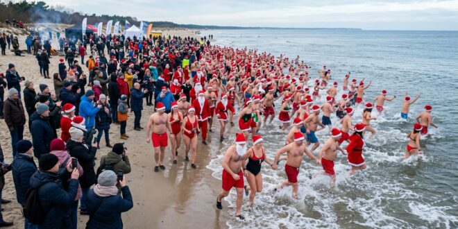 Morsujący Mikołajowie w czerwonych czapkach wchodzący do zimnego Bałtyku na plaży w Świnoujściu